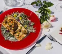 Salmon dish with greens on a red plate, surrounded by flowers on a white tablecloth.