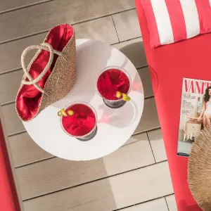 Two red drinks on a table with a straw bag and magazine on a red sunbed nearby.
