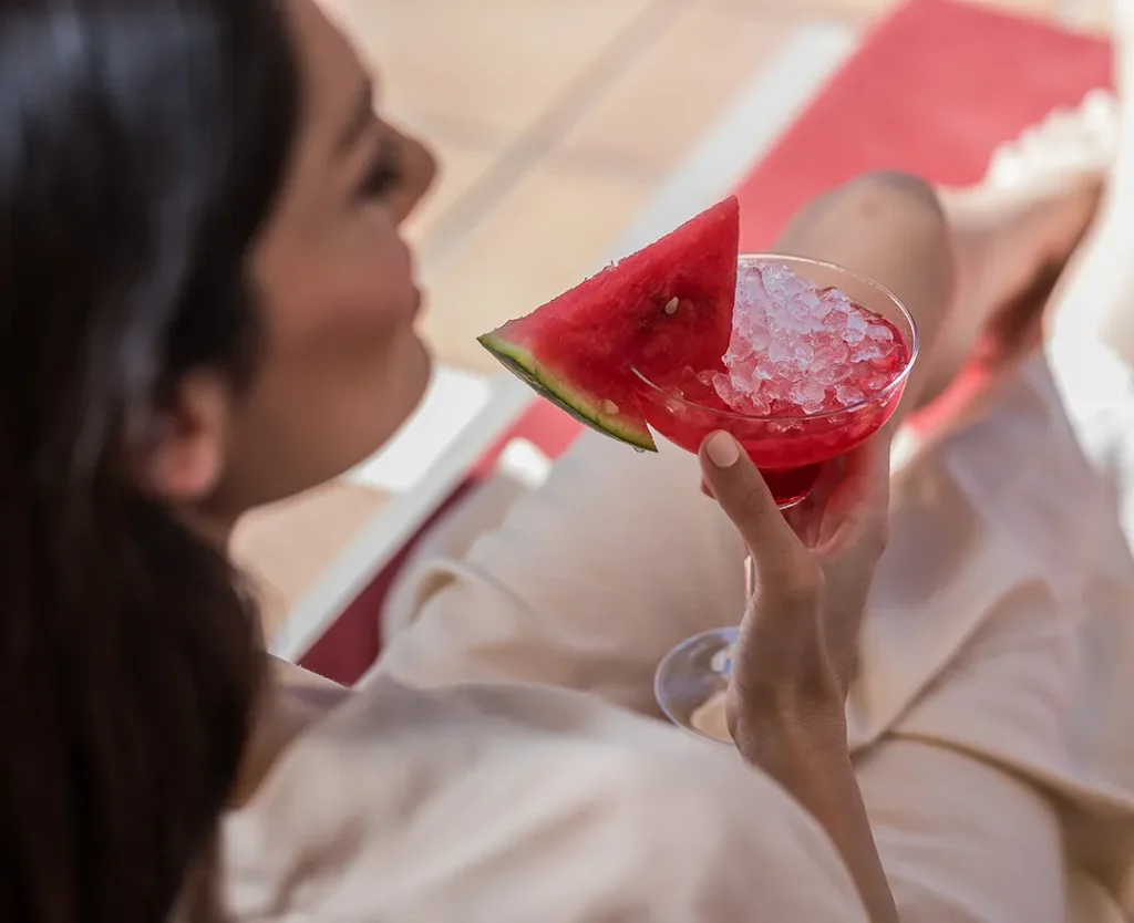 Woman lounging with a watermelon cocktail garnished with crushed ice.