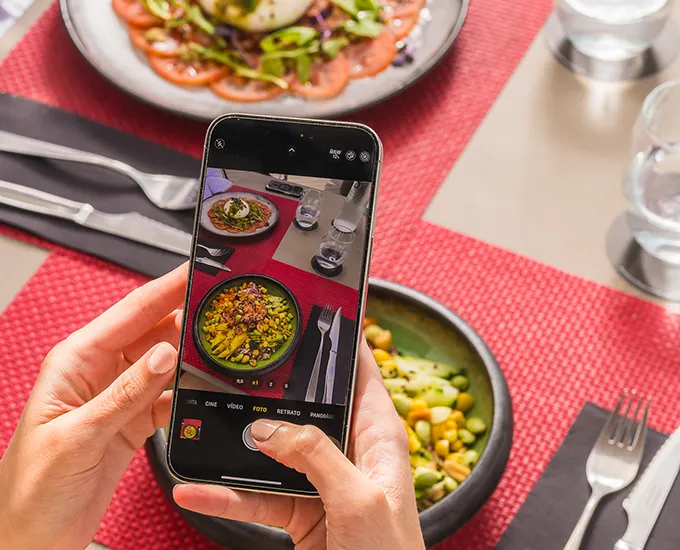 Hands using a phone to photograph a colorful salad on a red placemat.