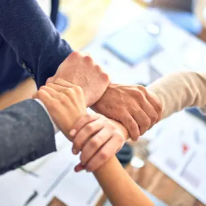 Four hands joined in a teamwork gesture over a desk with papers.