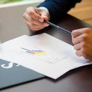 Hands holding a pen over a document with a colorful bar graph on a desk.