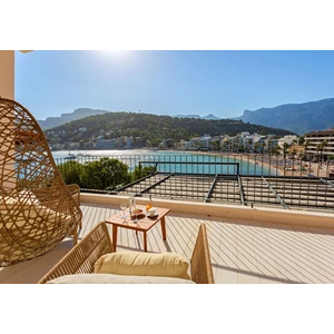 Sunny balcony with seating, overlooking a bay and mountains in the distance.