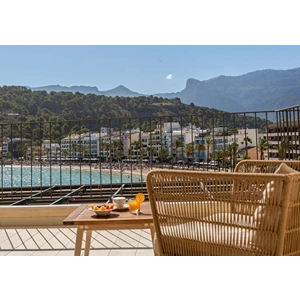 Outdoor seating with a table, fruit, and drink, overlooking a coastal town with mountains in the background.