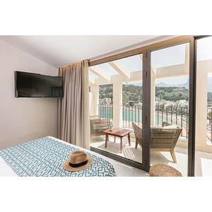 Hotel room with a balcony view, chairs, and a hat on bed.