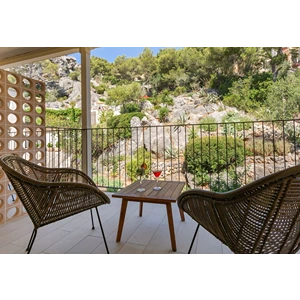 Two chairs and a table on a balcony overlooking green hills in sunny weather.