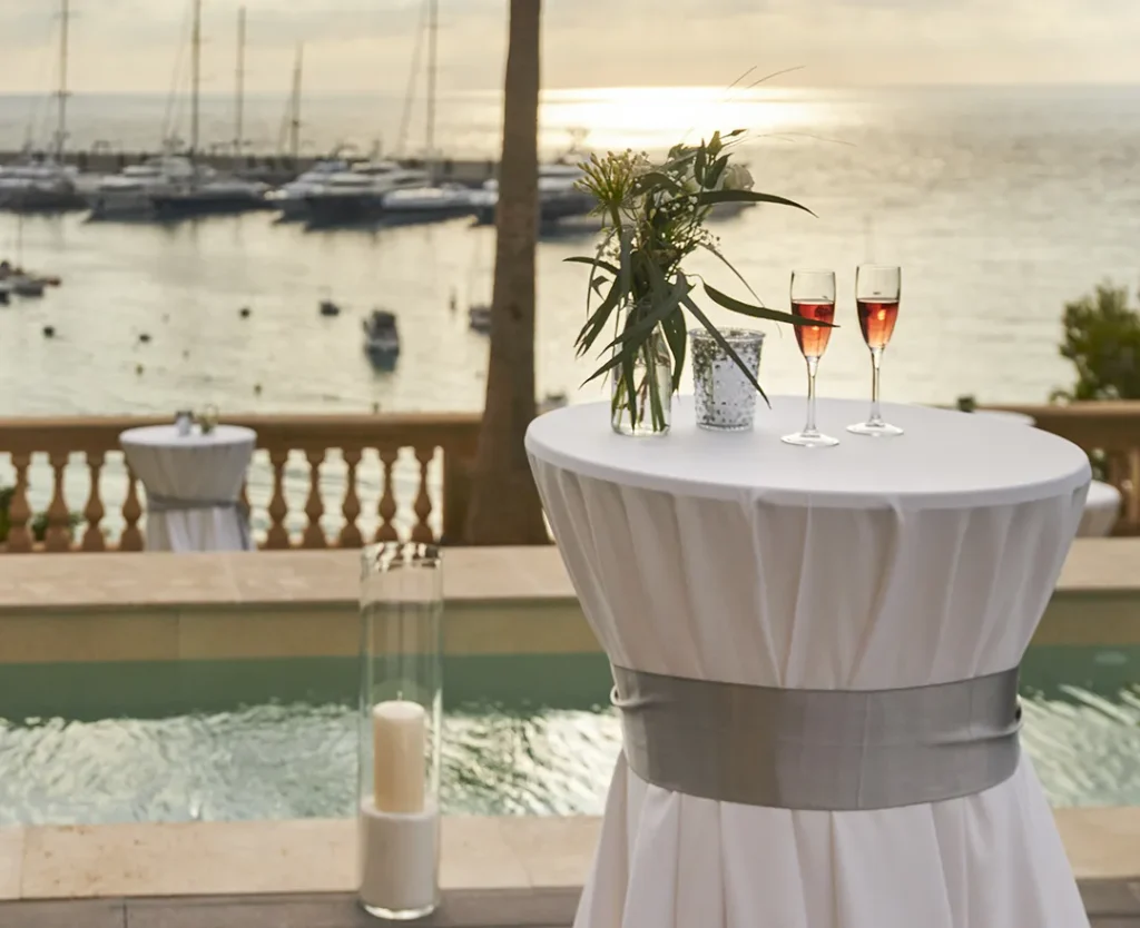 Cocktail table with flowers and drinks by a pool overlooking a marina at sunset.