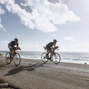 Cyclists riding on a coastal road under a cloudy sky.