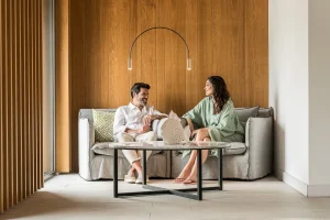 Couple sitting on a sofa, smiling at each other, with a fish sculpture on a coffee table.