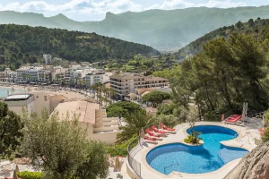Mountain view with pool, red loungers, and a coastal town nestled in lush greenery.