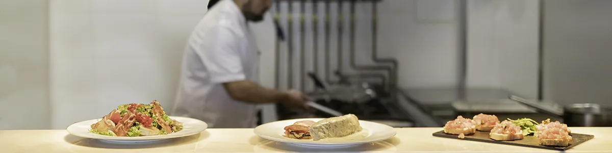 Plates of food on a counter with a chef cooking in the background.