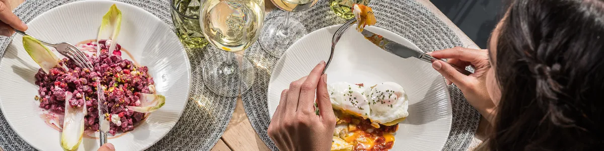 Two people dining on colorful dishes with glasses of white wine.