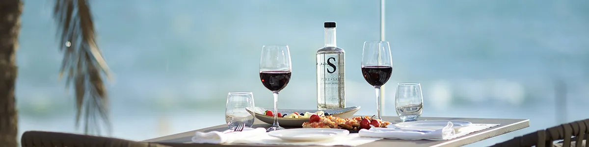 Outdoor table with wine, water, and appetizers by the sea.