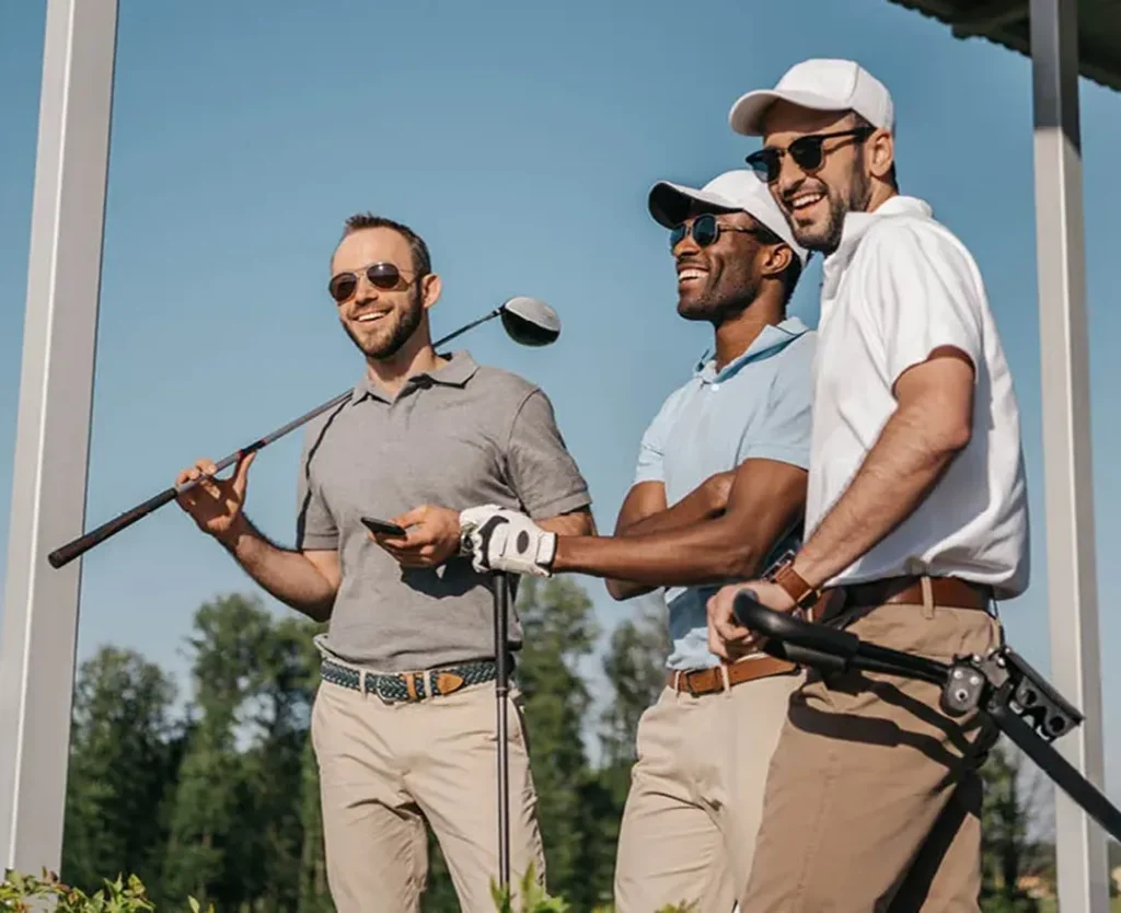 Three men standing outdoors with golf clubs, wearing casual golf attire and sunglasses.