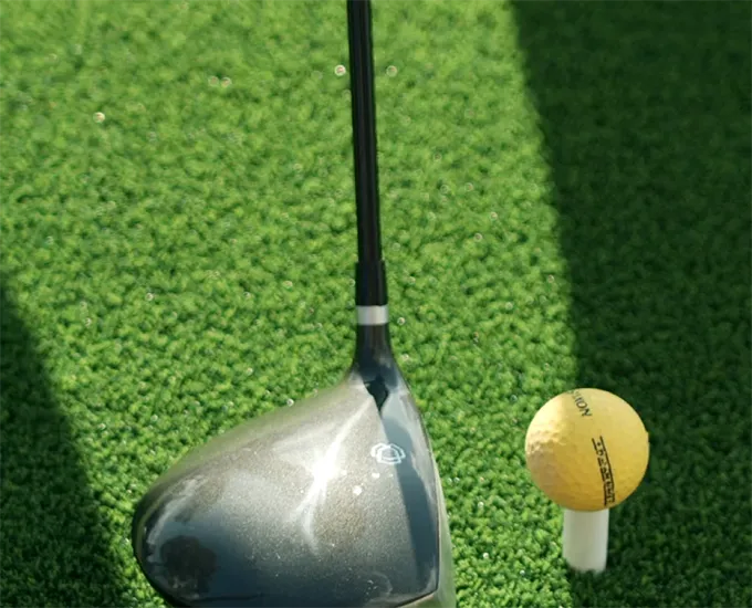Golf club near a yellow golf ball on green grass.
