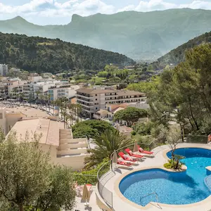 Aerial view of a pool with red chairs, surrounded by mountains and a town.