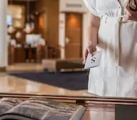Person holds a card with "S" in a lobby, standing near a display table with an open book.