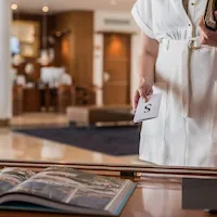 Person in white dress holding card near table with open book.