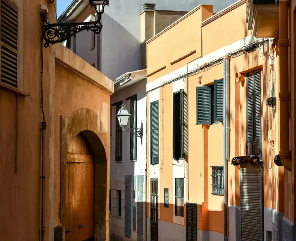 Narrow street with colorful buildings, lampposts, and shuttered windows in bright sunlight.