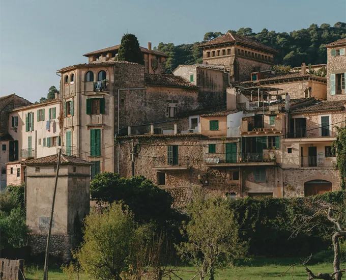 Rustic stone buildings with green shutters in a hillside village.