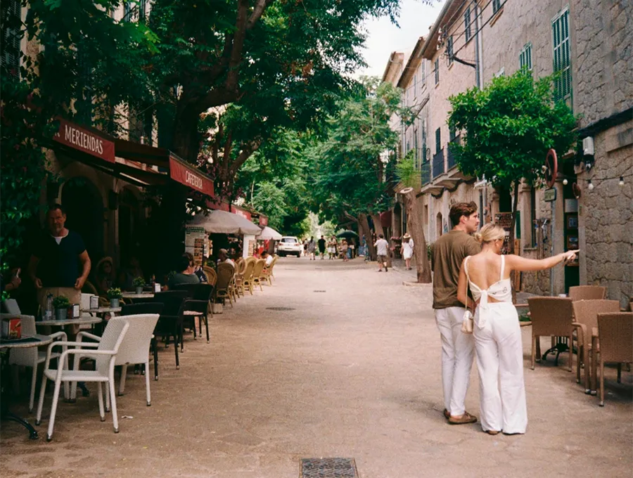 Couple exploring a charming street with outdoor café seating and greenery.