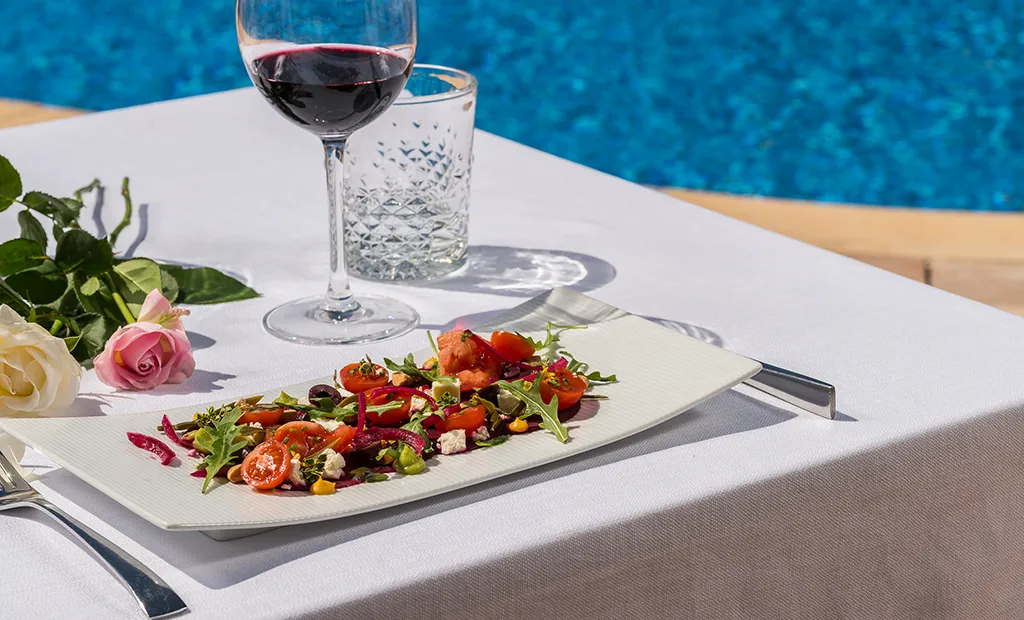 Salad and wine on a table by the pool, with roses placed nearby.