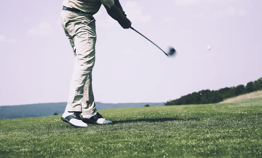 Golfer swinging on a lush green course under a clear sky.