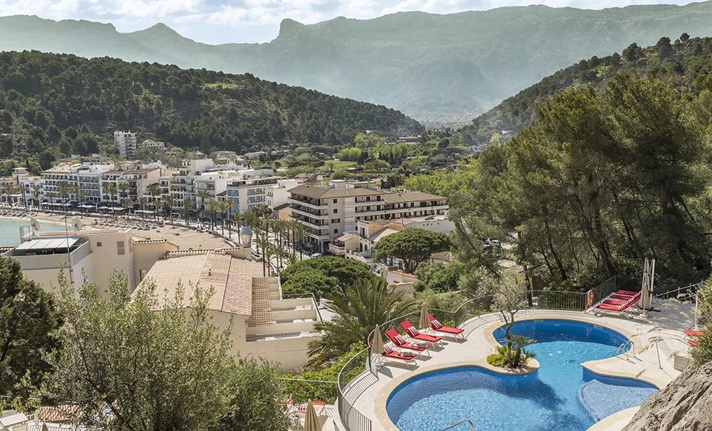 Aerial view of a coastal town with a pool, surrounded by hills and greenery.