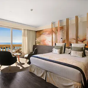 Modern hotel room with a large bed, seating area, and ocean view through the window.