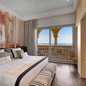 Hotel room with a bed, artwork, and a balcony view of the sea.