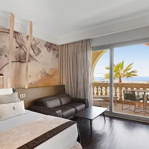 Hotel room with ocean view, balcony, bed, sofa, and abstract wall art.