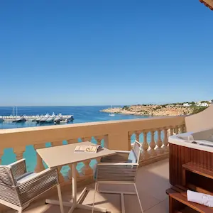 Coastal balcony view with table, chairs, and hot tub overlooking ocean and pier.
