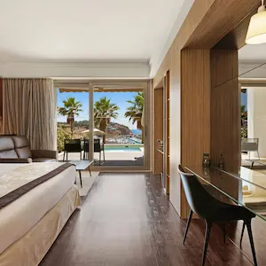 Hotel room with a view of palm trees and sea through sliding glass doors.
