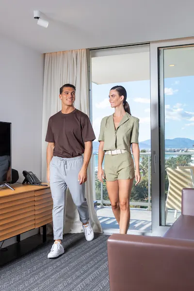 A man and woman walk in a bright room with large windows and a view of trees and mountains in the background.