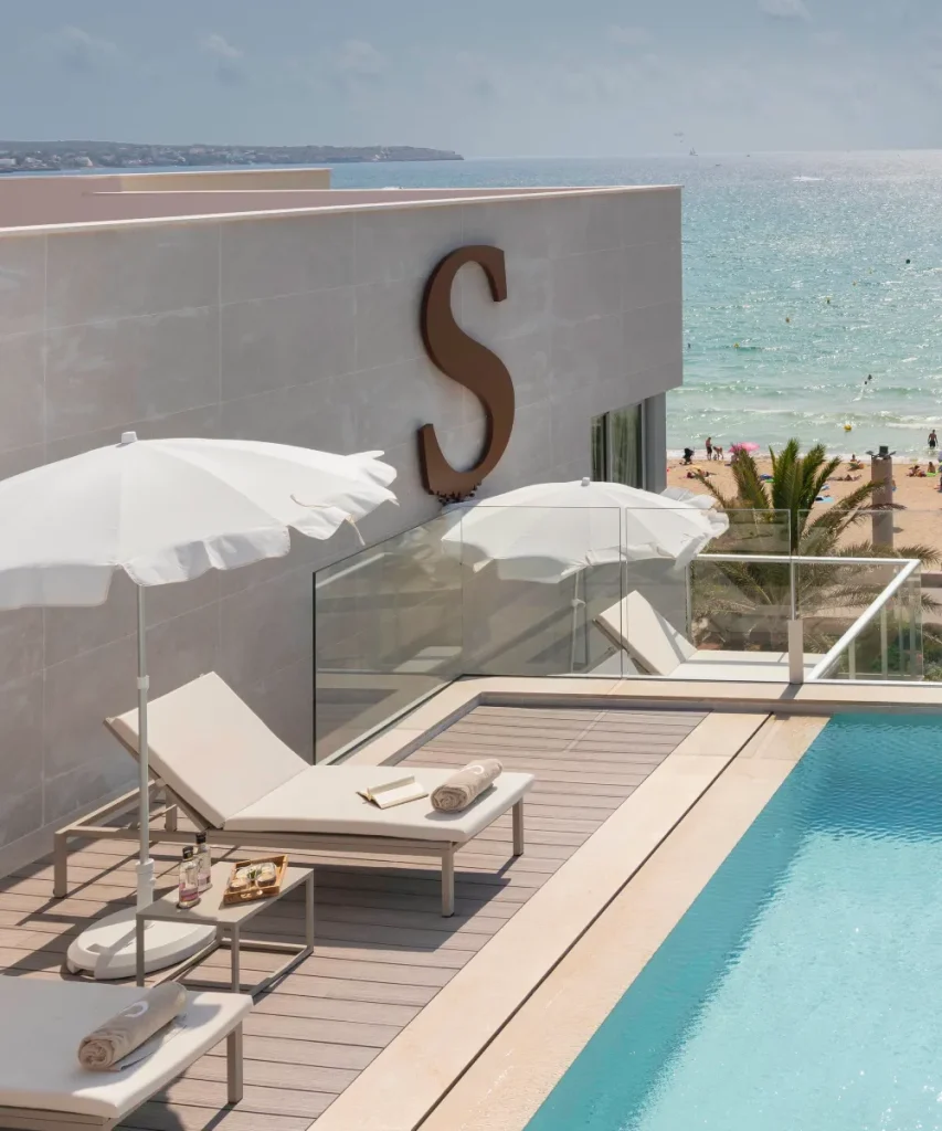 Rooftop pool with lounge chairs overlooks a beach and ocean under a sunny sky.