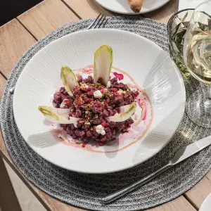 Elegant plate of beet salad with greens, served on a textured mat with a glass of white wine.