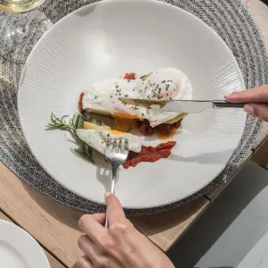 Person cutting poached eggs on toast with sauce, garnished with herbs.