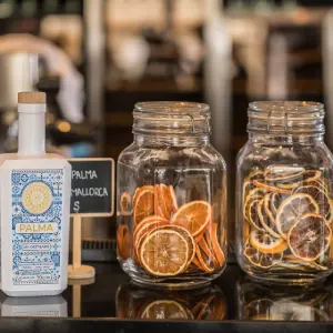 Gin bottle and jars of dried citrus slices on a counter.