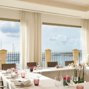 Elegant dining room with sea view, set tables, large windows, and soft lighting.