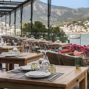 Outdoor restaurant with set tables, mountain view, and waterfront scenery in the background.