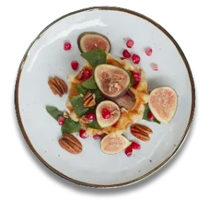 Waffle topped with figs, pecans, greens, and pomegranate on a white plate.