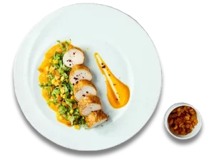 Plated chicken with vegetables and sauce; side of raisins in a small dish.