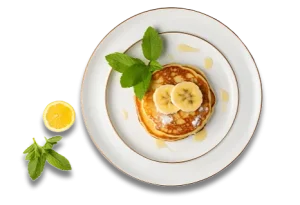 Pancakes with banana slices, mint leaves, lemon wedge, and syrup on a plate.