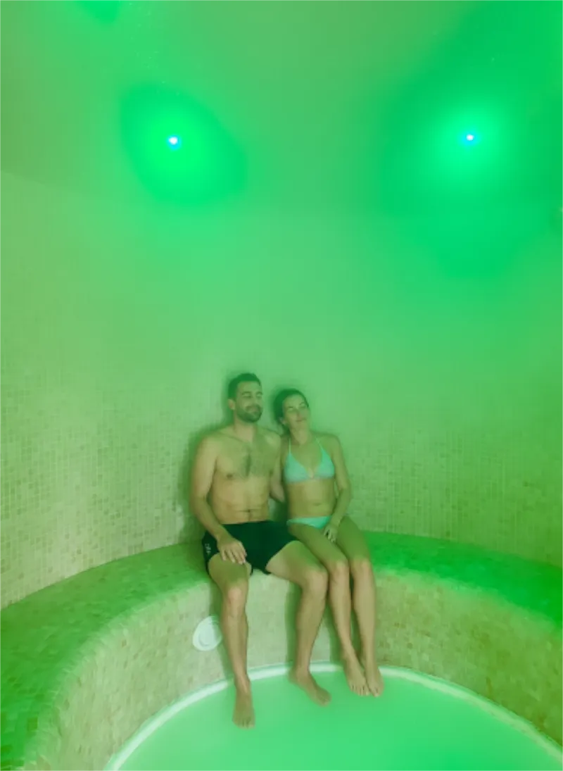 Personas relaj&aacute;ndose en una sala de vapor iluminada con luces verdes.