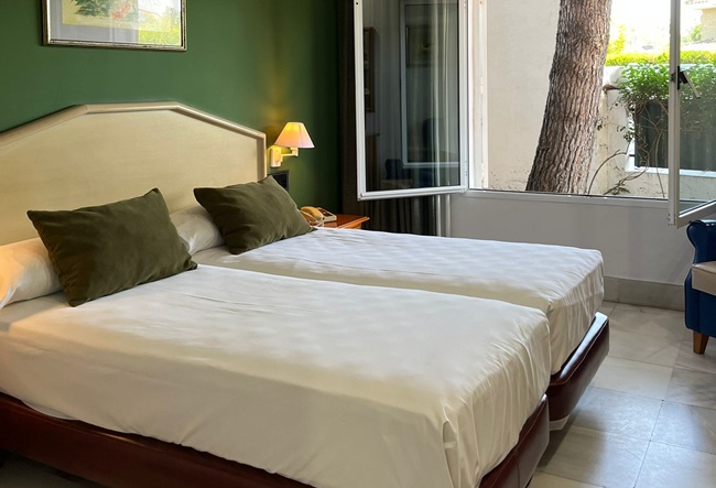 Dos camas individuales en habitaci&oacute;n con pared verde y ventana abierta.