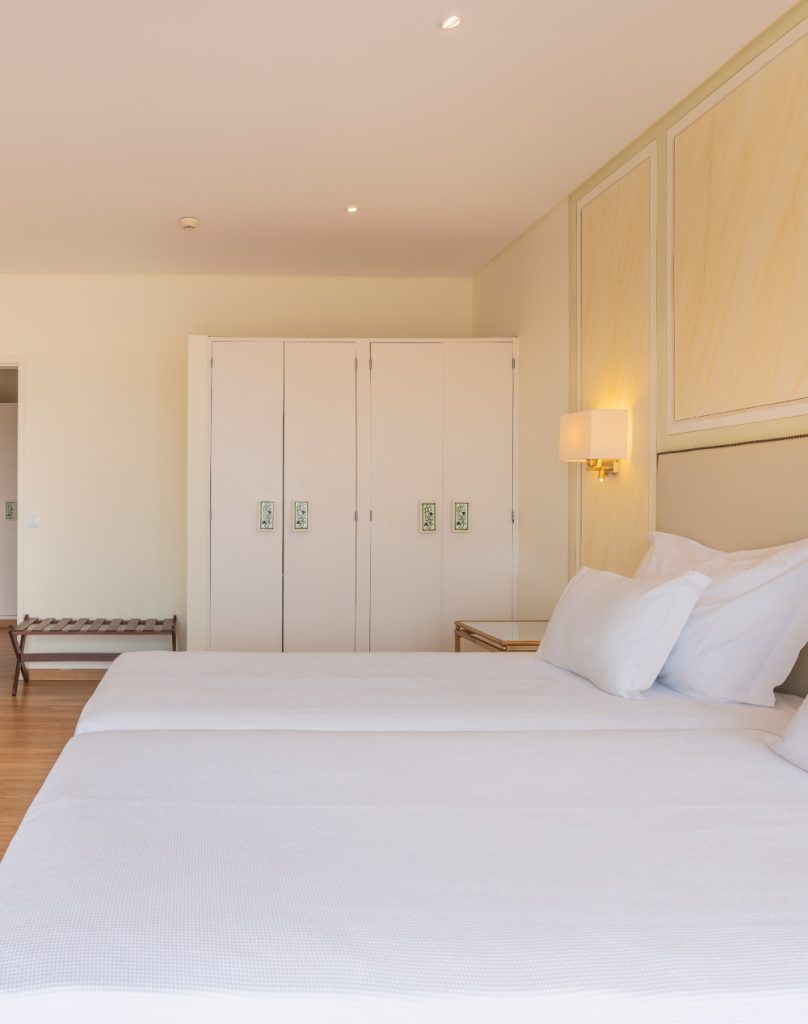 Minimalist bedroom with a neatly made bed, white wardrobes, and a warm wall sconce.