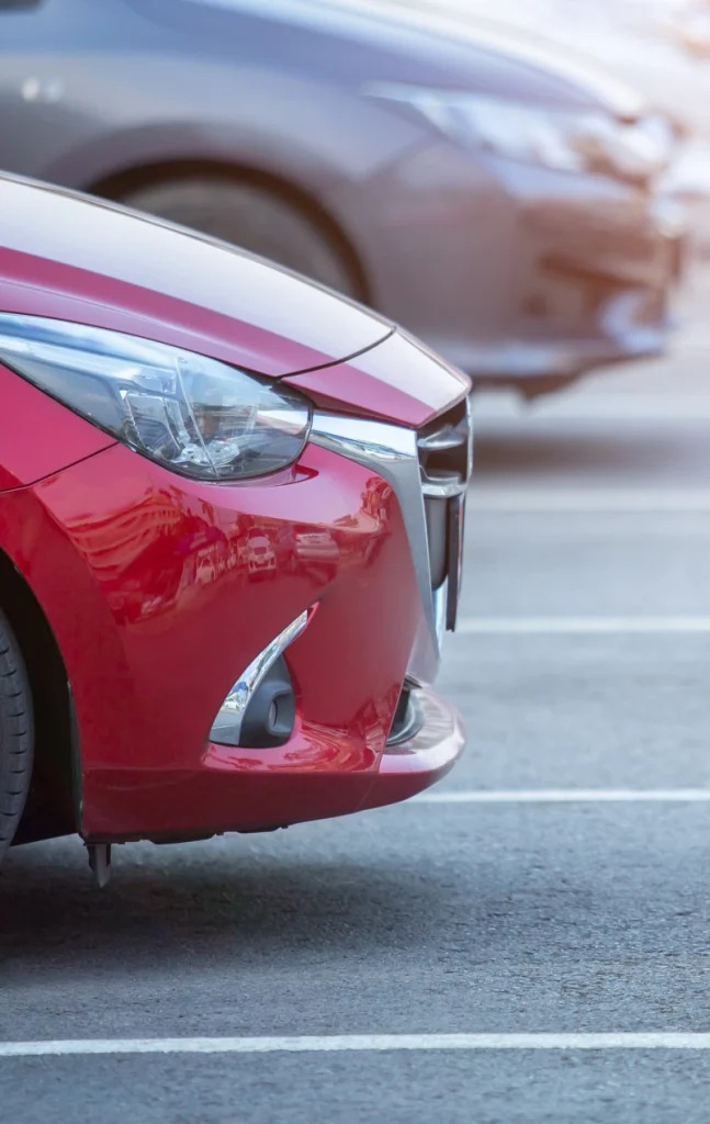 Close-up of a red car in a parking lot, with a blurred gray car in the background.