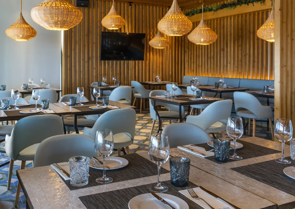 A stylish restaurant interior with wooden accents, modern furniture, and warm lighting from hanging lamps.