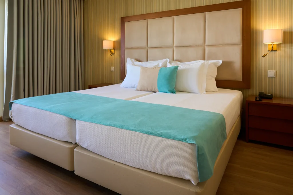 Hotel room with a double bed, teal accents, beige headboard, and bedside lamps.