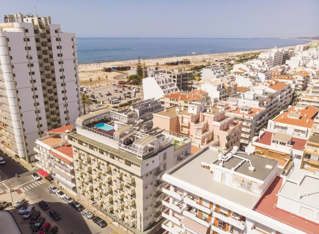 Aerial view of beachfront city with hotels, rooftop pool, and ocean in the background.